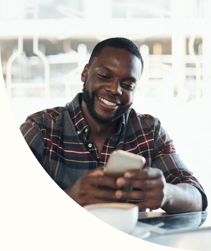 handsome young african man sitting alone in a cafe using his cellphone