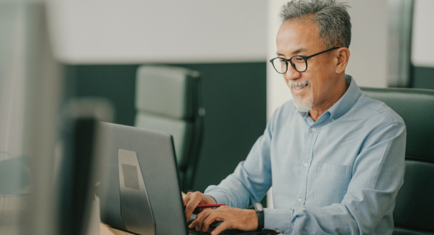 Asian man using laptop typing working in office open plan