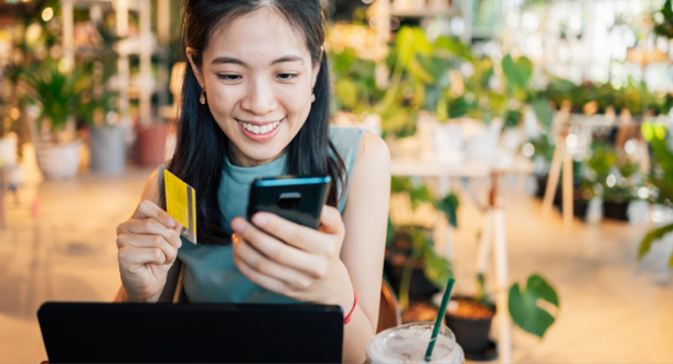 Asian woman shopping with credit card holding smartphone with smiling face on blurred shopping mall background